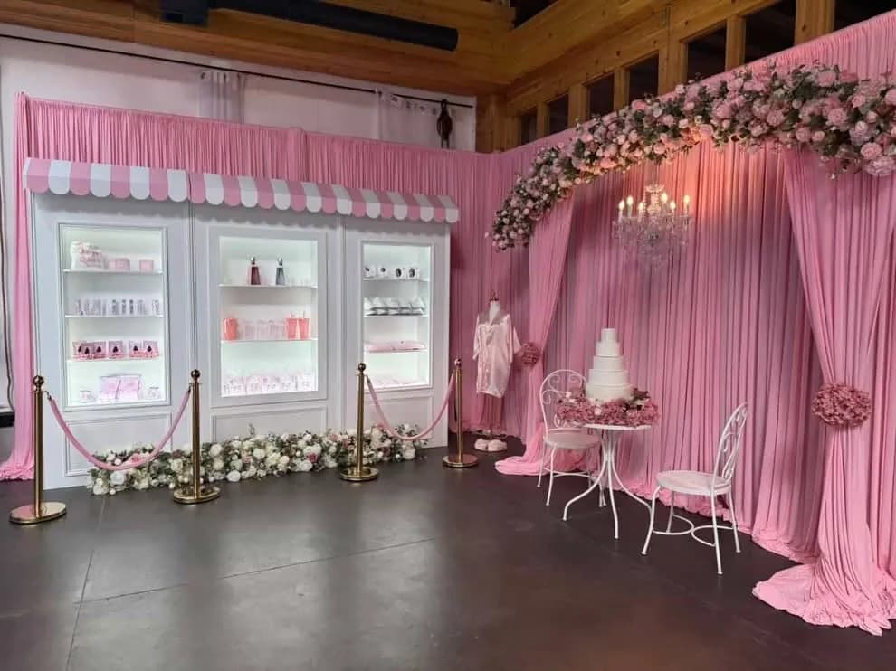 Pink draped candy shop backdrop with lit display cases, gold stanchions, a floral arch with chandelier and a four tier cake