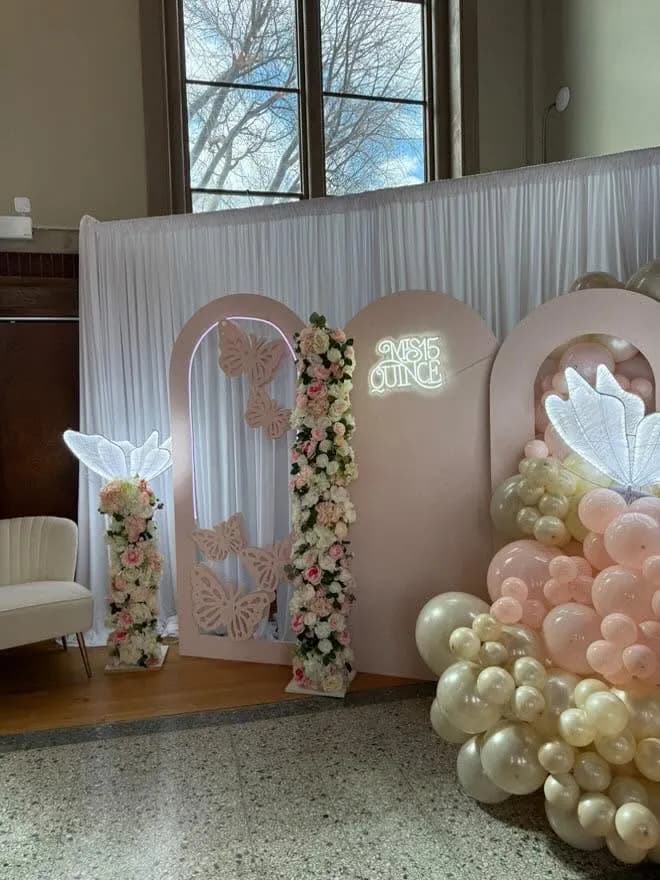 Blush pink quinceanera arches with cut butterflies, a Mis 15 Quince neon sign, floral column and blush balloon garland