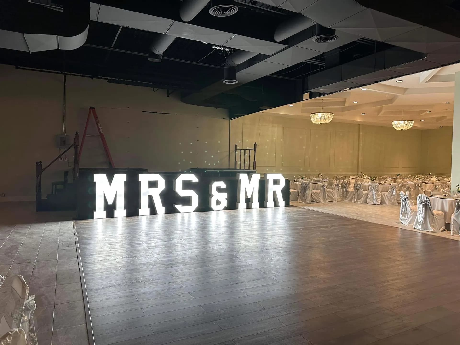 Giant light-up MRS & MR marquee letters glowing beside a ballroom dance floor, with white and silver dressed tables behind