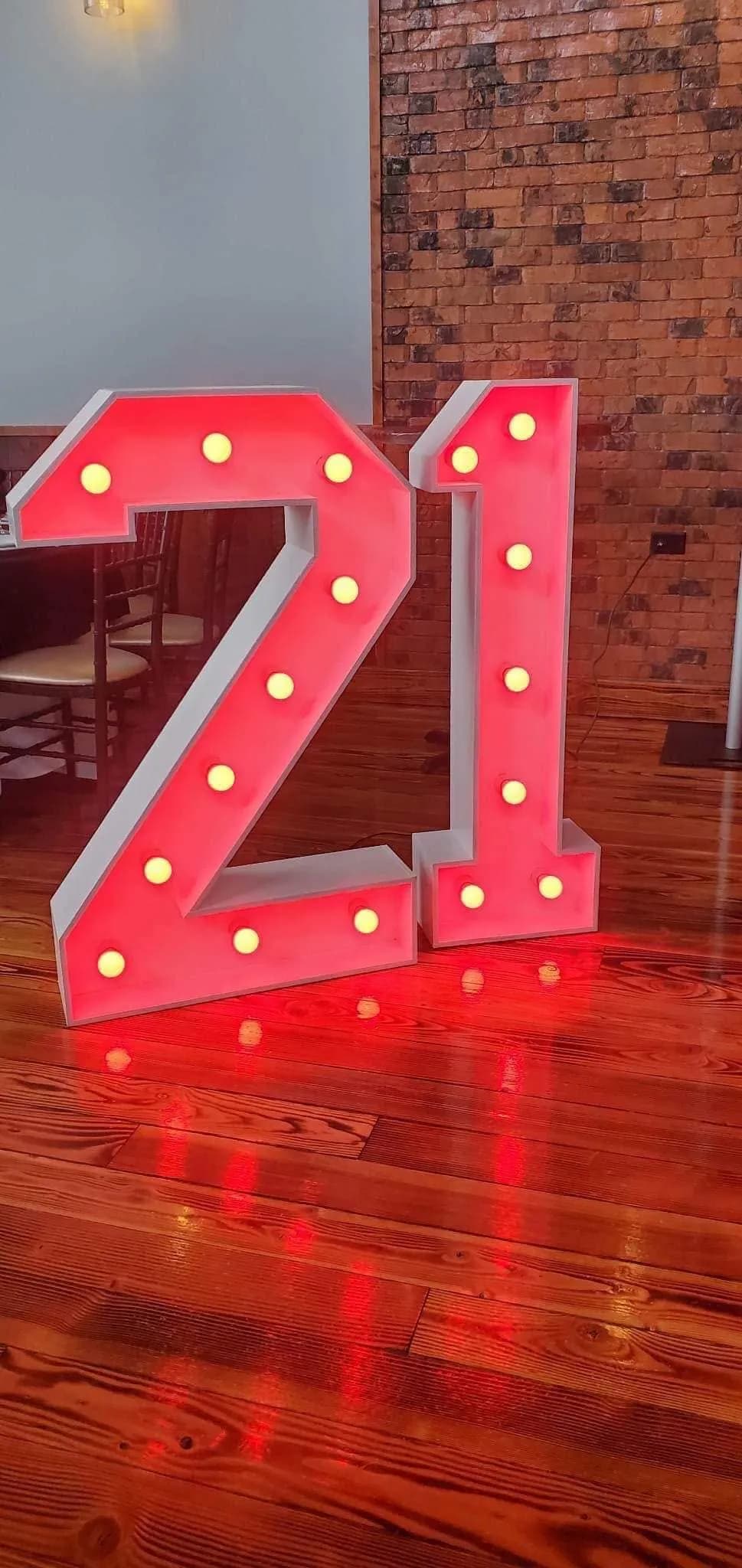 Giant light-up marquee number 21 lit in red on a polished wood floor against an exposed brick wall