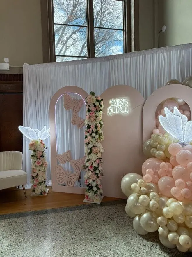 Blush pink quinceanera arches with cut butterflies, a Mis 15 Quince neon sign, floral column and blush balloon garland