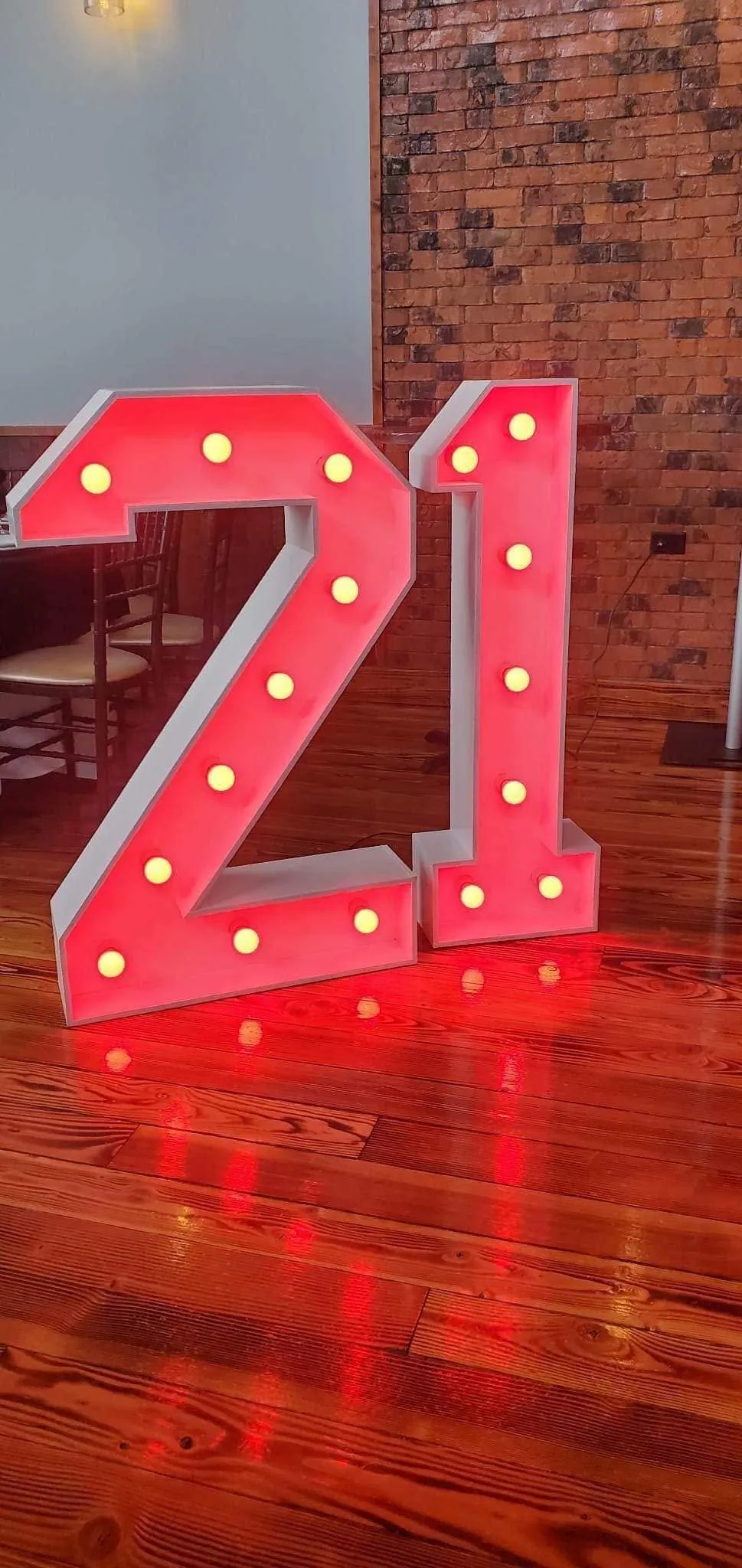 Giant light-up marquee number 21 lit in red on a polished wood floor against an exposed brick wall